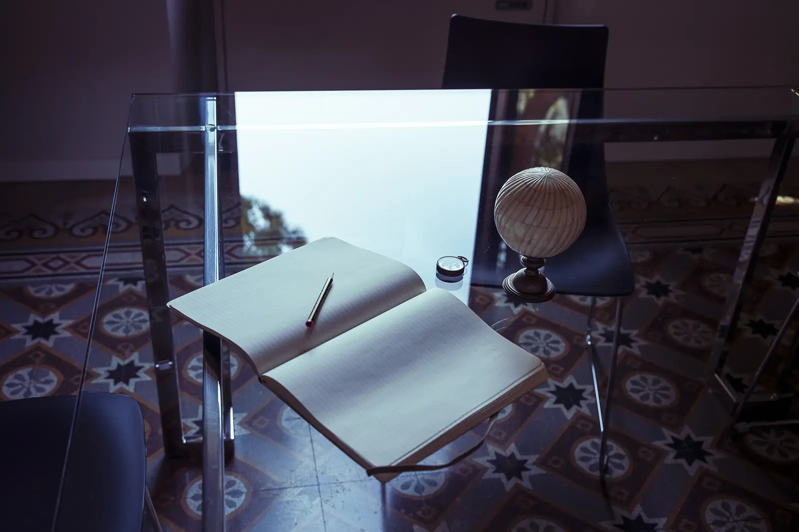 Scrivania in vetro dello Studio con un quaderno aperto e un mappamondo in legno